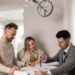 Couple discussing a blueprint with a real estate agent, planning their new home purchase.