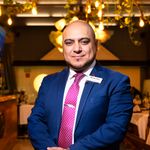 Portrait of a confident businessman in a restaurant, elegantly dressed in a blue suit and pink tie.